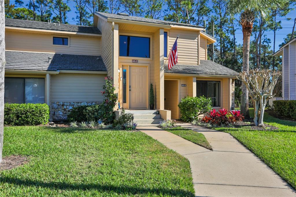 A two-story tan townhouse with a concrete walkway, a front door, and an American flag — 149 BLUE HERON DRIVE UNIT D, DAYTONA BEACH, FL