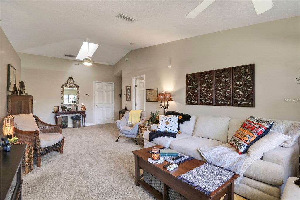 A living room features a beige sofa, wicker armchair, coffee table, and decorative wall panels — 149 BLUE HERON DRIVE UNIT D, DAYTONA BEACH, FL