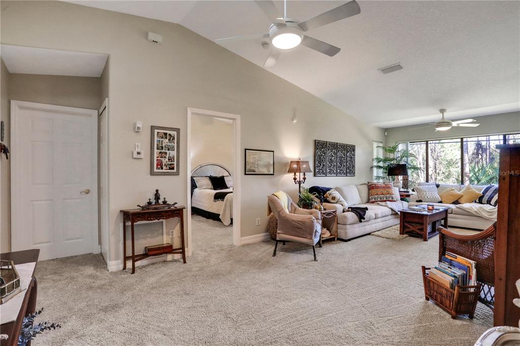 A living room with vaulted ceilings, beige carpeting, and a doorway leading to a bedroom — 149 BLUE HERON DRIVE UNIT D, DAYTONA BEACH, FL