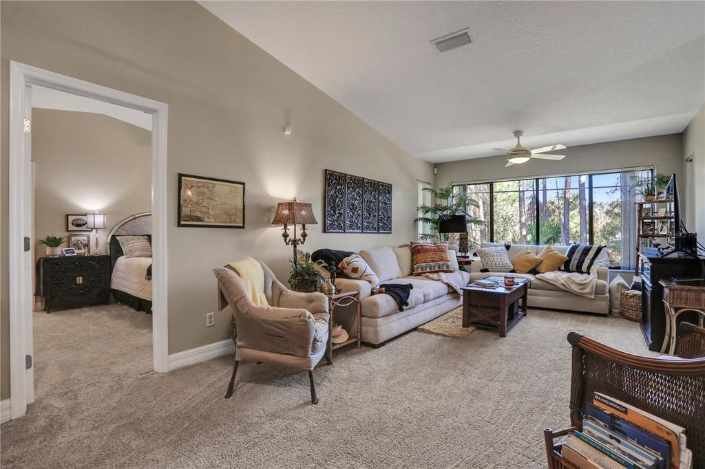 A living room with beige carpet, a sectional sofa, and an adjacent bedroom doorway — 149 BLUE HERON DRIVE UNIT D, DAYTONA BEACH, FL