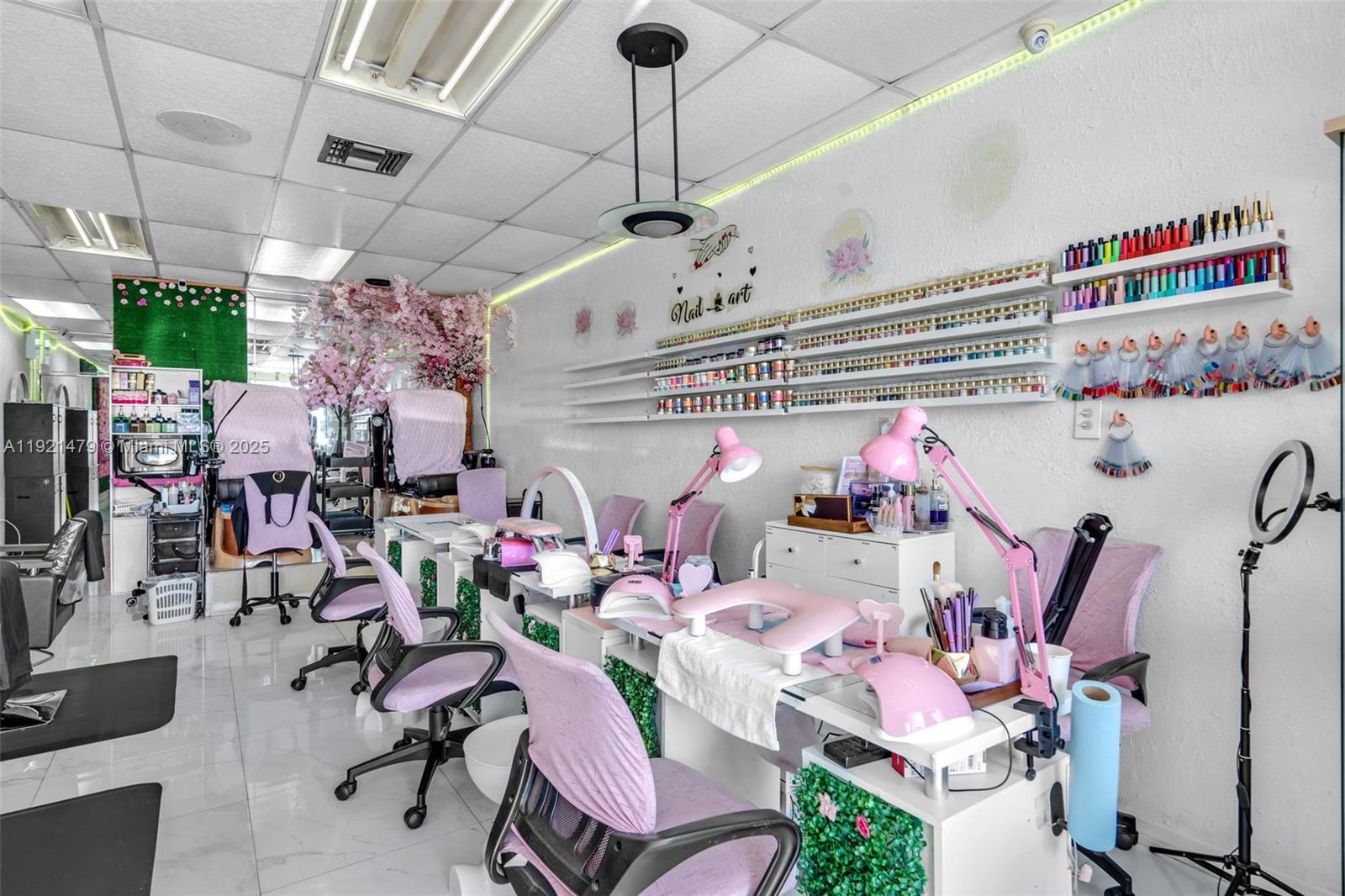 A nail salon interior features multiple manicure stations with pink chairs, lamps, and wall-mounted polish displays — 6761 W Flagler St, Miami FL 33144, MIAMI, FL