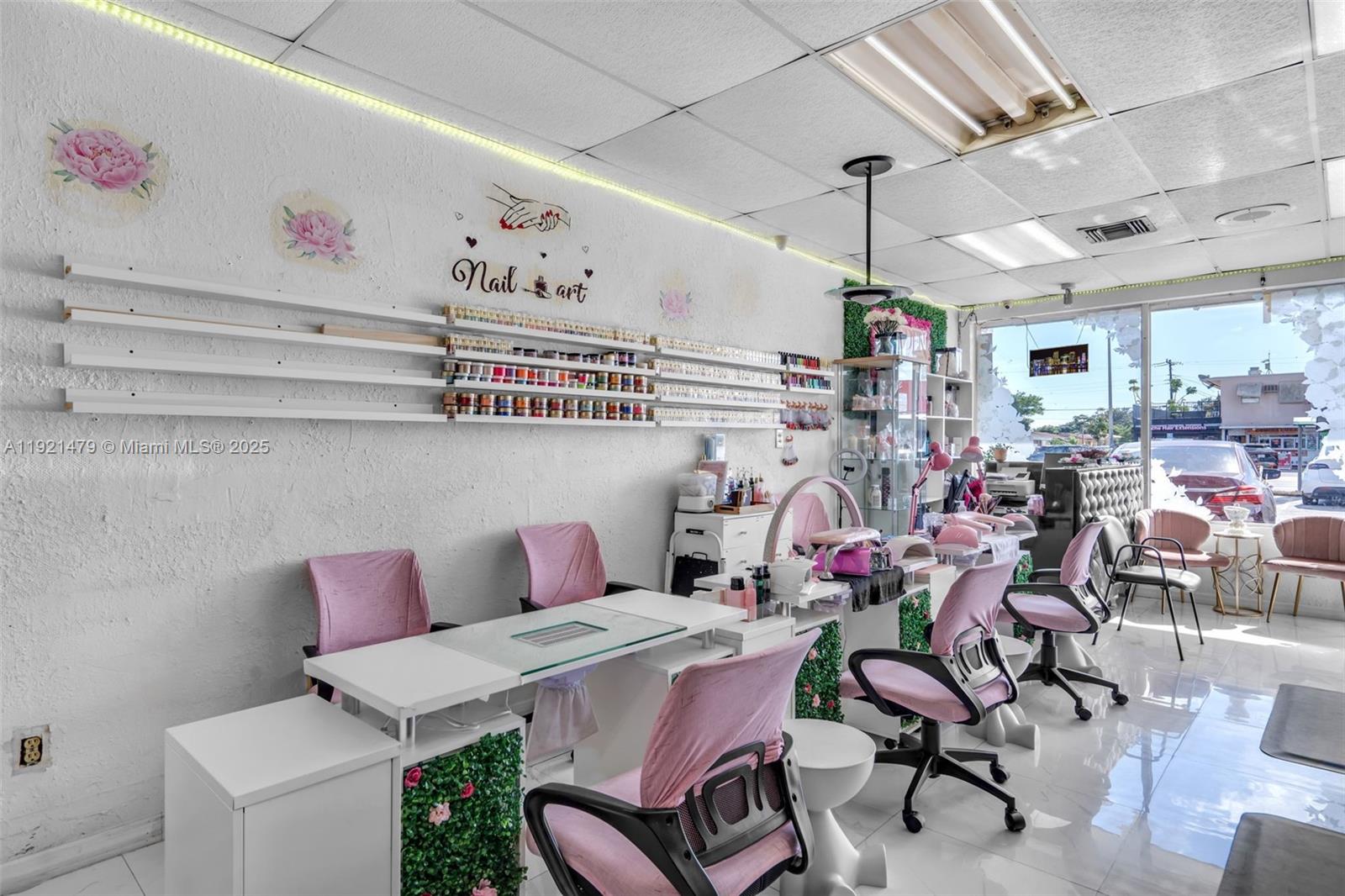 A bright nail salon features white workstations, pink chairs, and wall-mounted shelves for polish — 6761 W Flagler St, Miami FL 33144, MIAMI, FL