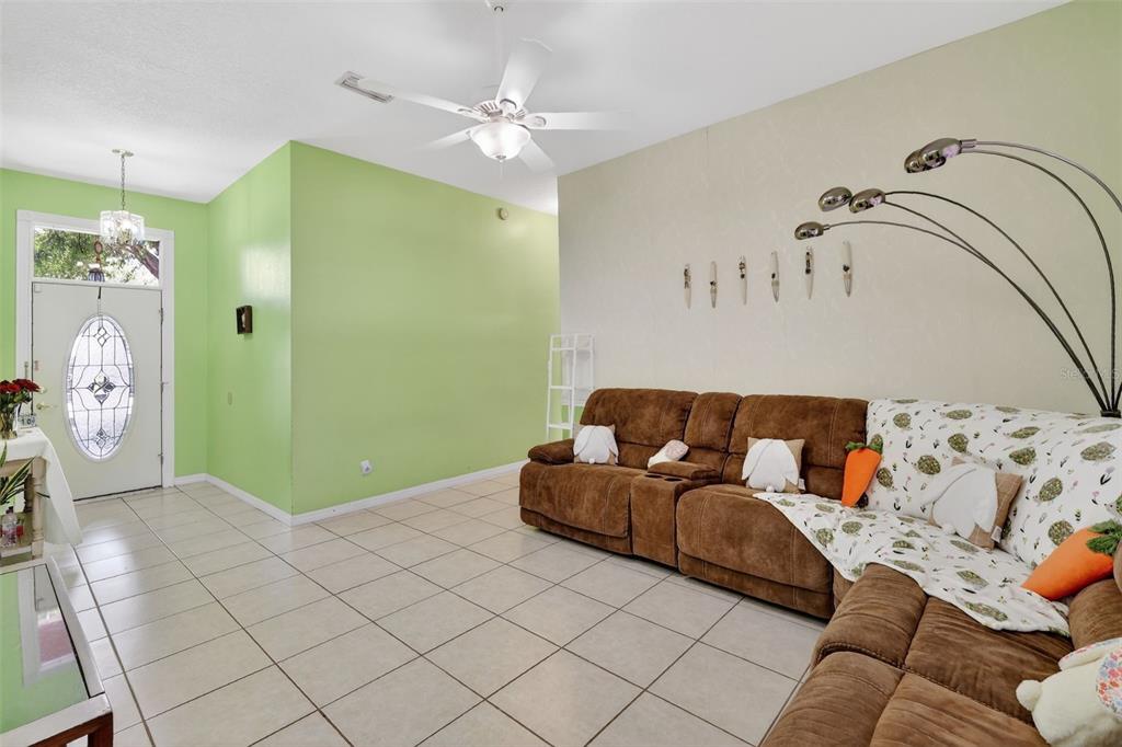 A living room features light green walls, beige tile floors, a ceiling fan, and brown furniture — 11318 SUMMER WIND COURT, CLERMONT, FL