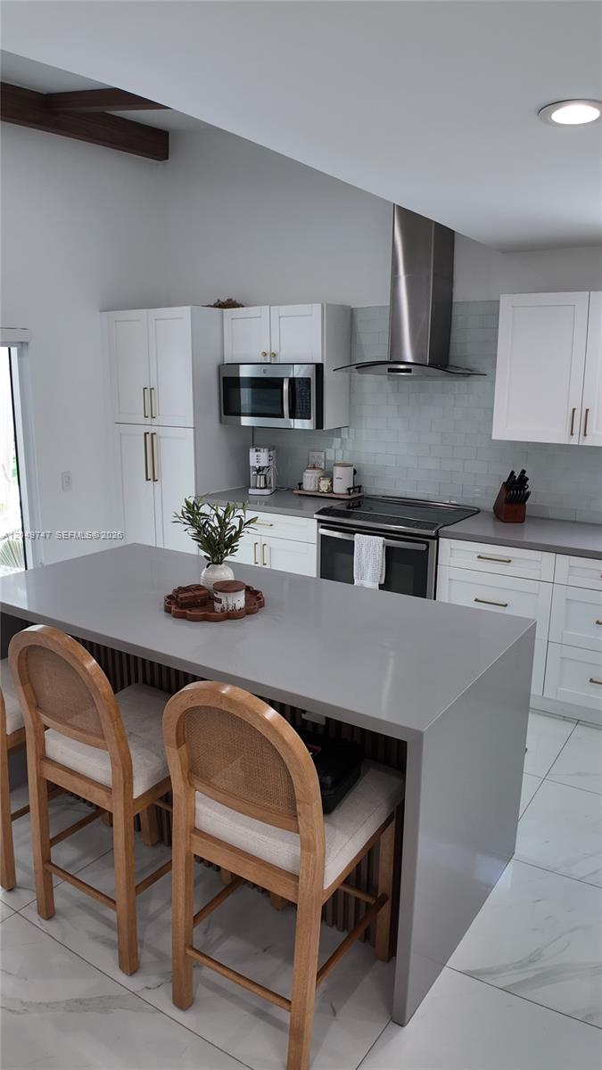 A modern kitchen features a gray waterfall island, white cabinetry, and stainless steel appliances — 14605 SW 142nd Pl, Miami FL 33186, MIAMI, FL