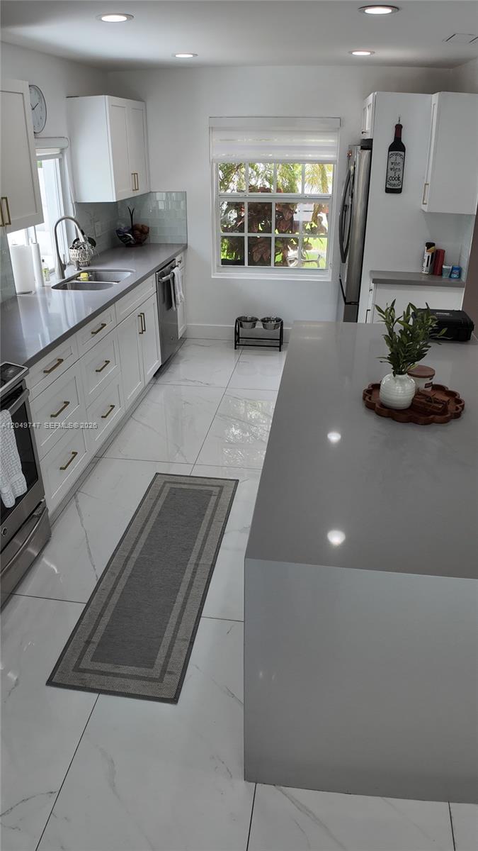 A modern kitchen features white cabinetry, gray countertops, a large island, and white tiled floors — 14605 SW 142nd Pl, Miami FL 33186, MIAMI, FL
