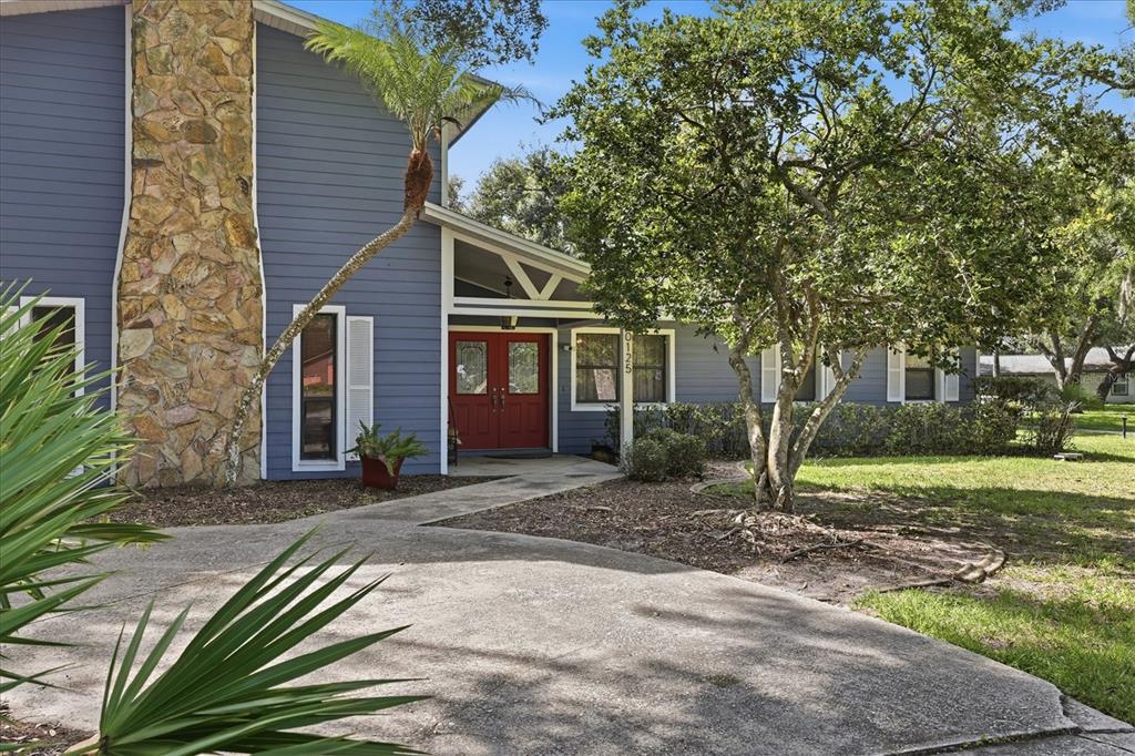 A blue house with a stone chimney, red double front doors, and a concrete driveway — 10125 OAK RUN DRIVE, BRADENTON, FL