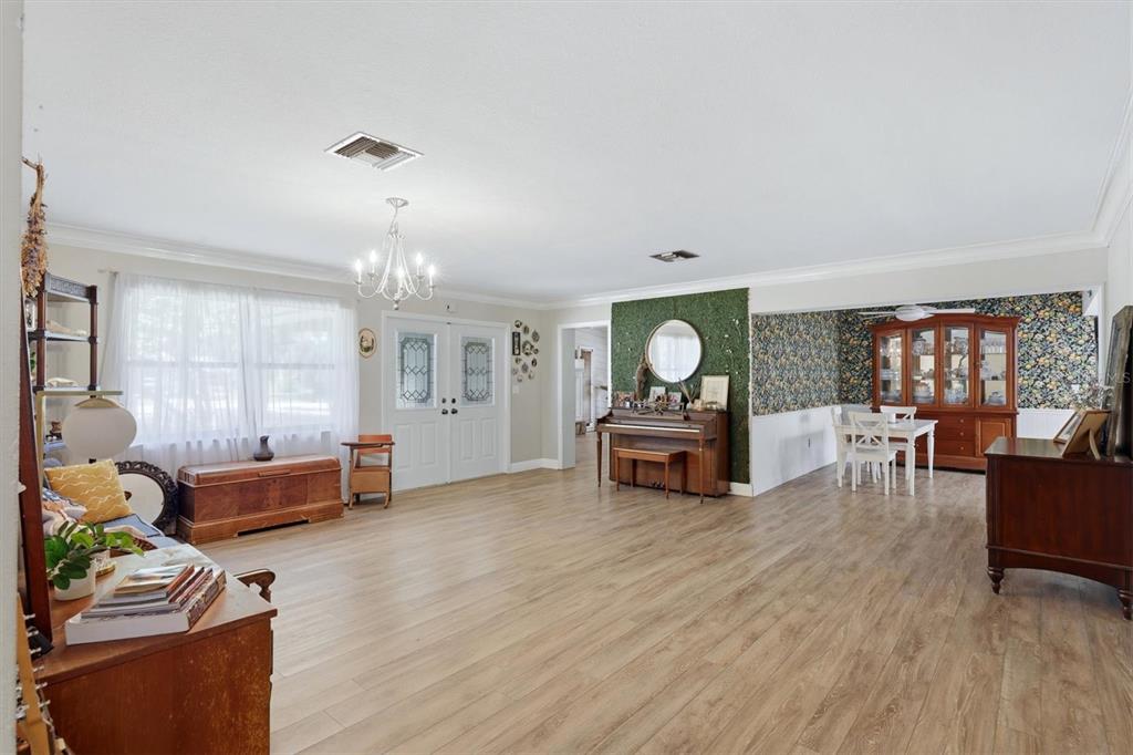 A living and dining area with wood-look flooring, a piano, and floral wallpaper — 10125 OAK RUN DRIVE, BRADENTON, FL