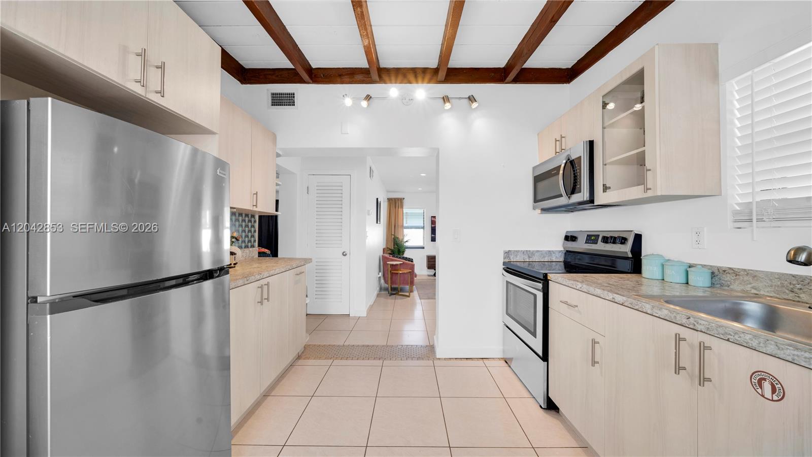 A kitchen features light wood cabinets, stainless steel appliances, and exposed wooden ceiling beams — 1704 Rodman St # 3, Hollywood FL 33020, HOLLYWOOD, FL
