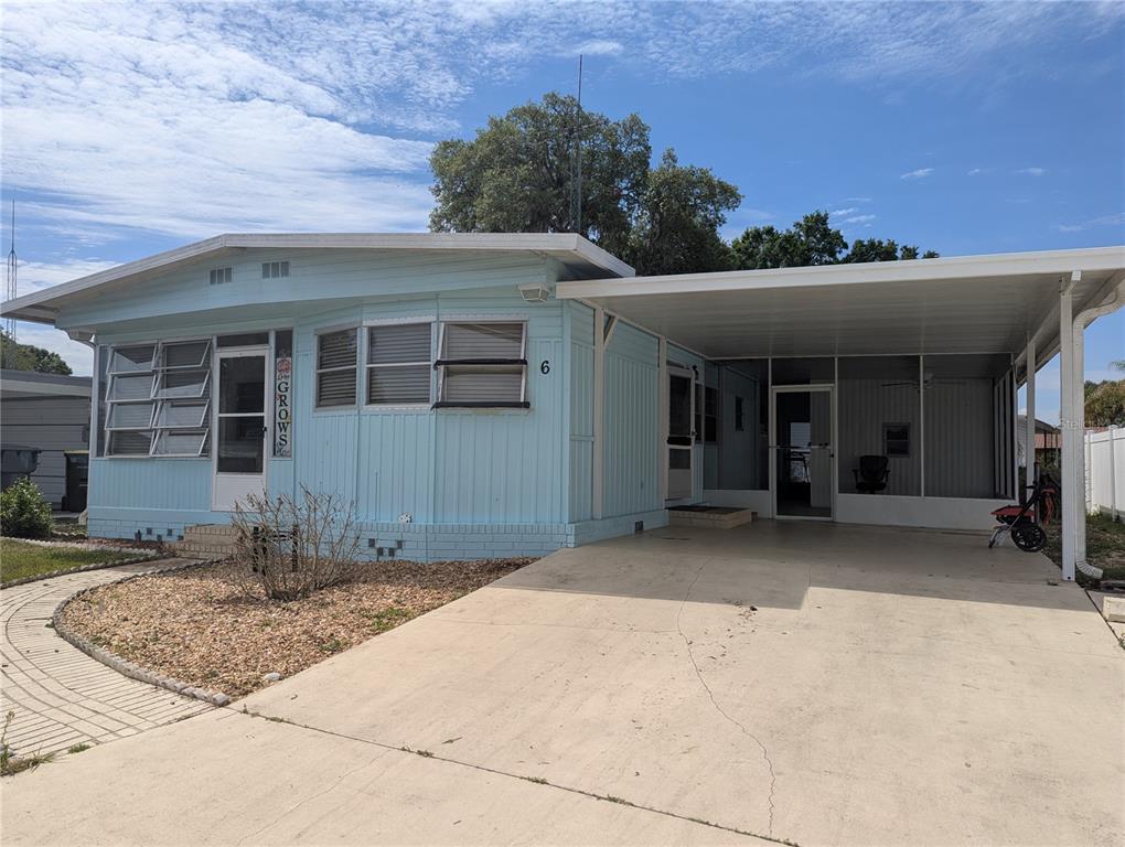 A light blue mobile home features a carport, a screened porch, and a gravel yard — 6 PINE LANE, HAINES CITY, FL