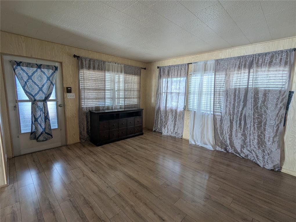 A living room features wood-look flooring, wood-paneled walls, and windows covered with curtains and blinds — 6 PINE LANE, HAINES CITY, FL