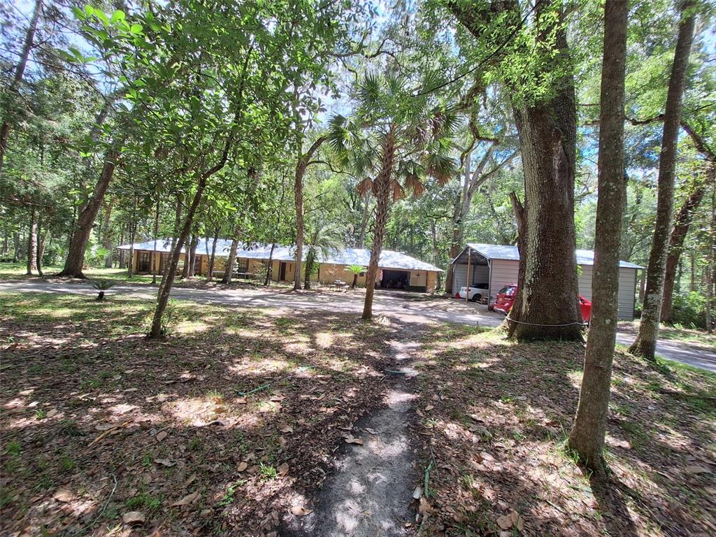 A single-story house with a metal roof and a detached carport sits among many trees — 11304 ROYAL DRIVE, BROOKSVILLE, FL