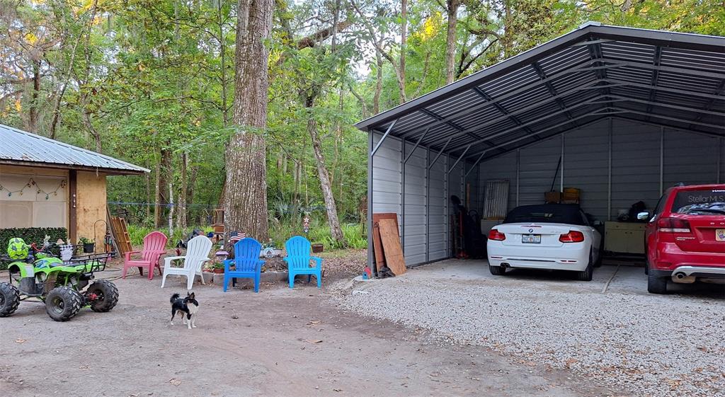 A gravel driveway leads to a metal carport with two parked cars and four chairs — 11304 ROYAL DRIVE, BROOKSVILLE, FL