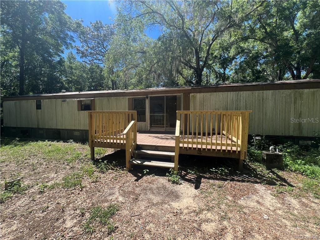 A single-wide mobile home features a wooden deck with stairs leading to sliding glass doors — 1660 S PALM AVENUE, HOMOSASSA, FL