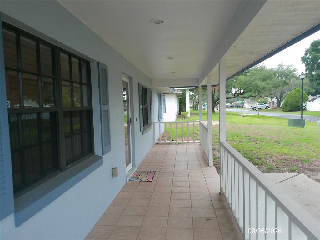 A covered front porch with tiled flooring, white railings, and a view of the yard — 1601 ARCHERS PATH, LAKELAND, FL