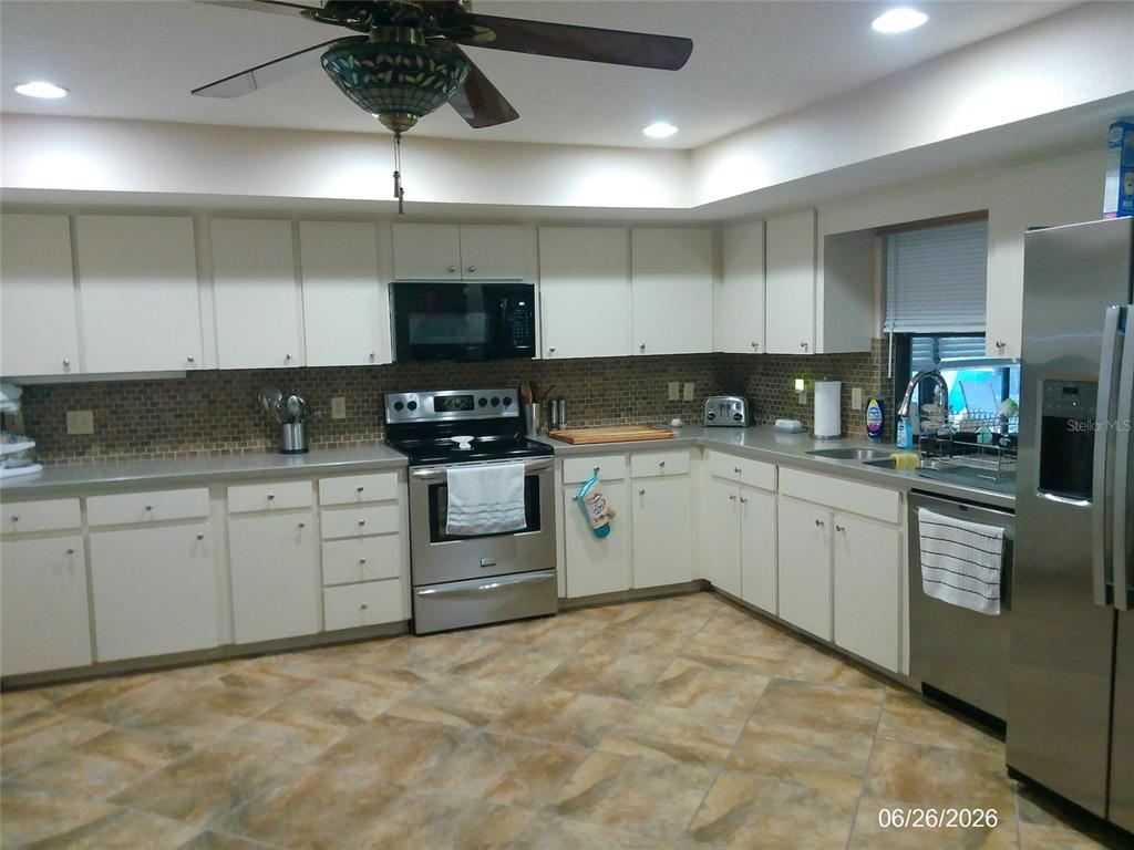 A kitchen features white cabinetry, stainless steel appliances, a tiled backsplash, and tile flooring — 1601 ARCHERS PATH, LAKELAND, FL