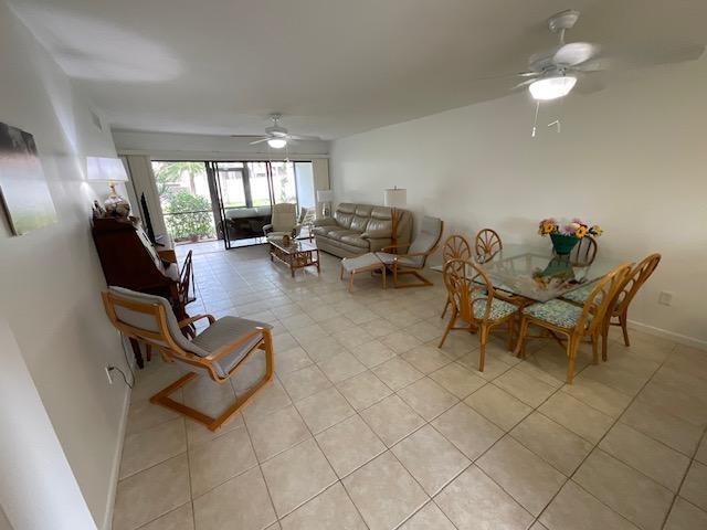 An open-concept living and dining area features tile flooring, a glass-top table, and sliding doors — 1600 NE Dixie Highway # 107, Jensen Beach FL 34957, JENSEN BEACH, FL