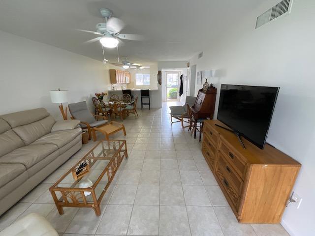 A living room with a beige sofa, glass coffee table, television, and dining area — 1600 NE Dixie Highway # 107, Jensen Beach FL 34957, JENSEN BEACH, FL