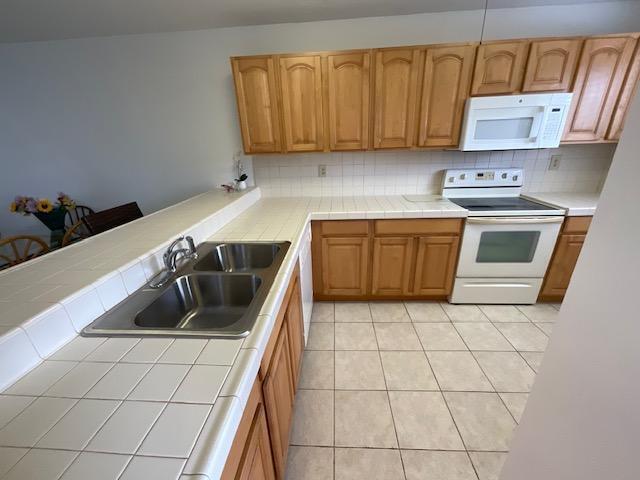 A kitchen features light wood cabinets, white tile countertops, and white appliances — 1600 NE Dixie Highway # 107, Jensen Beach FL 34957, JENSEN BEACH, FL