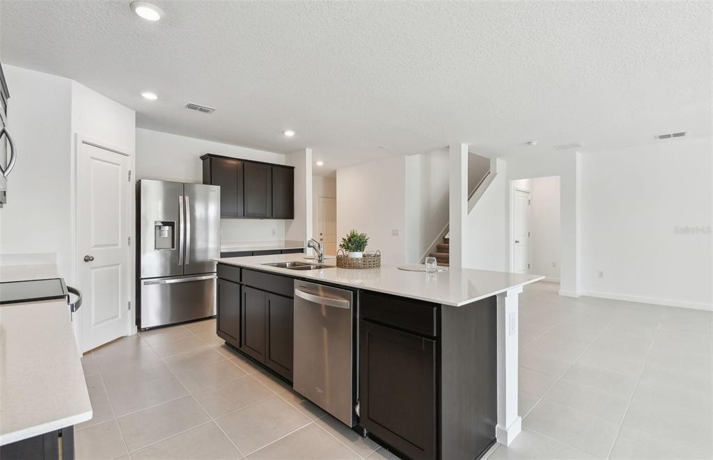 A modern kitchen features dark cabinetry, stainless steel appliances, and a large white quartz island — 10818 SAPPHIRE BREEZE COVE, PARRISH, FL