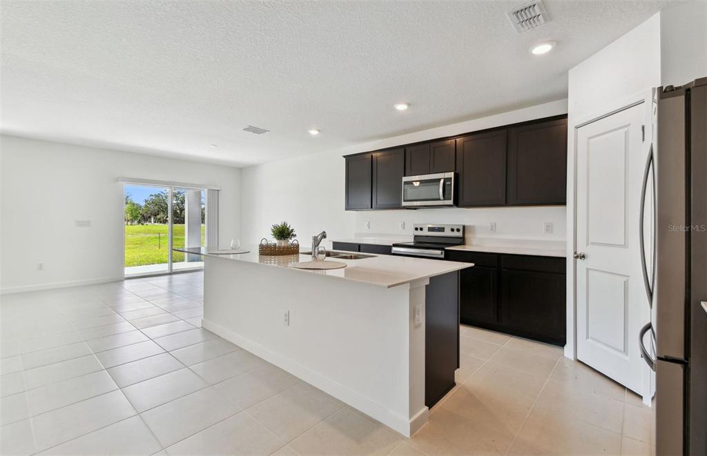 A kitchen features dark cabinets, white countertops, a center island, and a sliding glass door — 10818 SAPPHIRE BREEZE COVE, PARRISH, FL