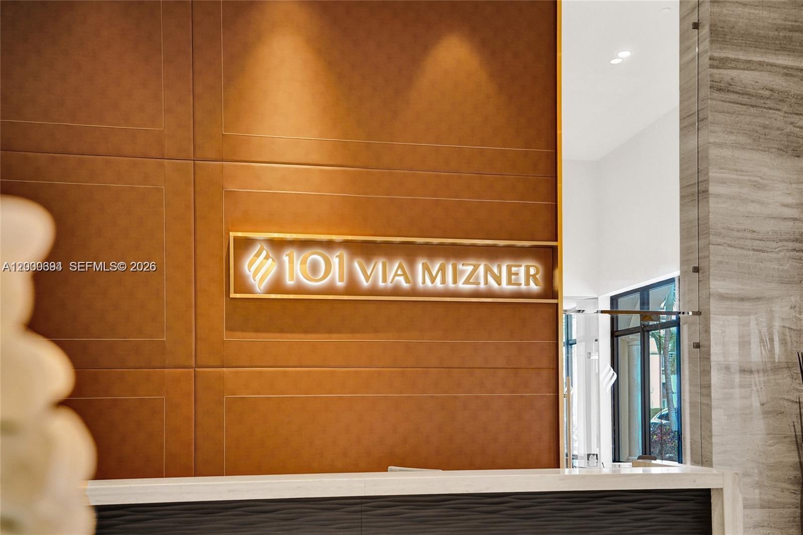A reception desk sits in front of a brown paneled wall with illuminated building signage — 101 E Camino Real # 517, Boca Raton FL 33432, BOCA RATON, FL