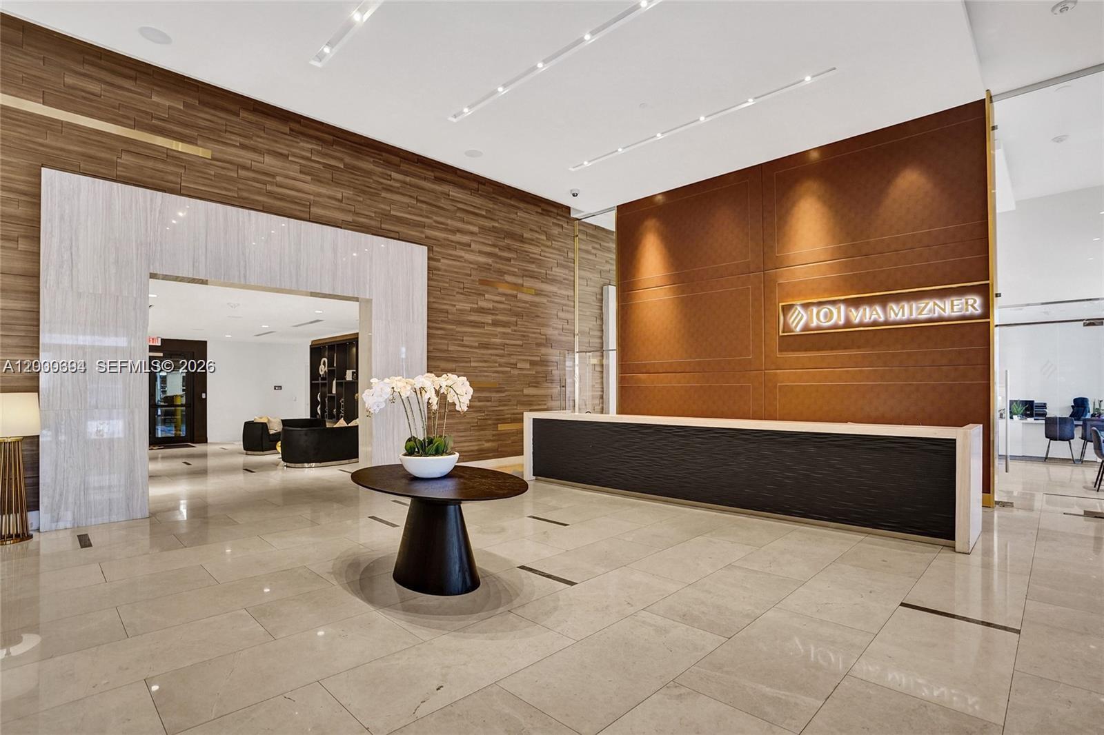 A modern lobby features a reception desk, wood-paneled walls, and a central floral arrangement — 101 E Camino Real # 517, Boca Raton FL 33432, BOCA RATON, FL