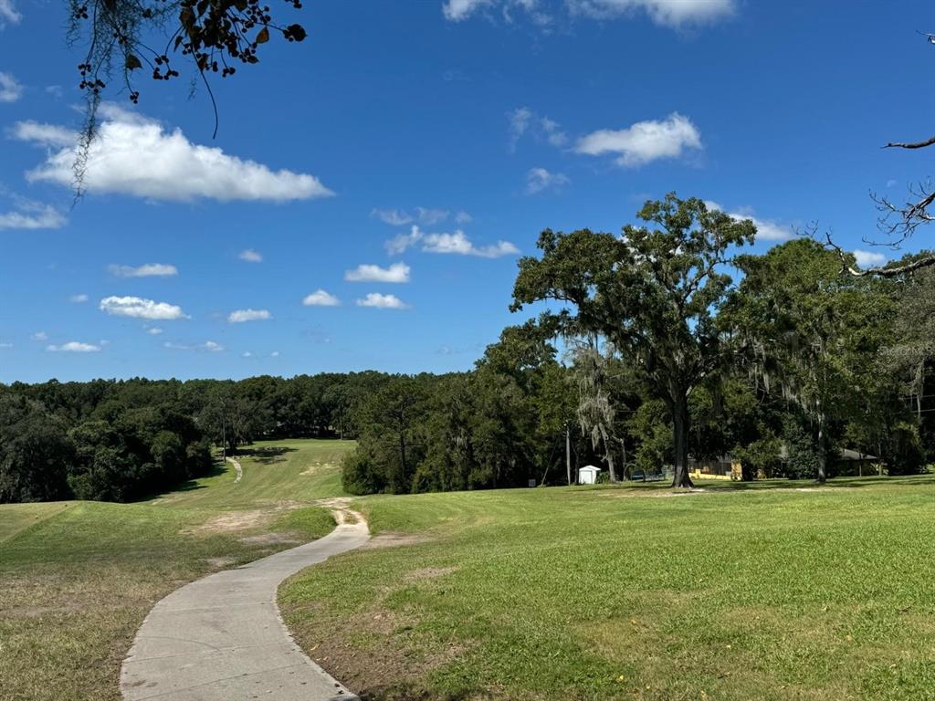 A paved path winds through a grassy golf course toward a line of trees — 60 E FALCON STREET, DUNNELLON, FL