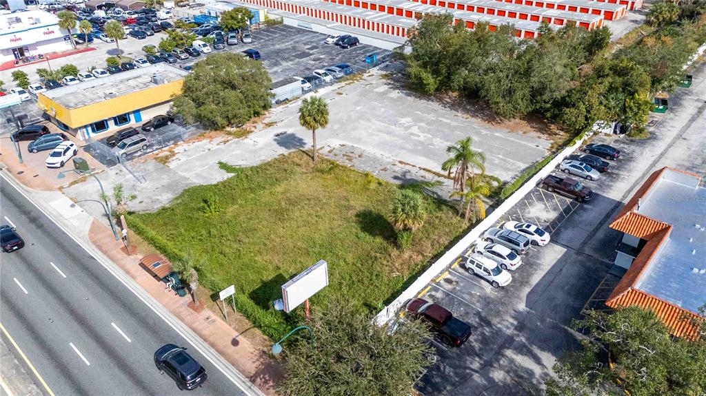 An aerial view shows a vacant, grassy lot situated between a commercial building and parking areas — 4849 S ORANGE BLOSSOM TRAIL, ORLANDO, FL