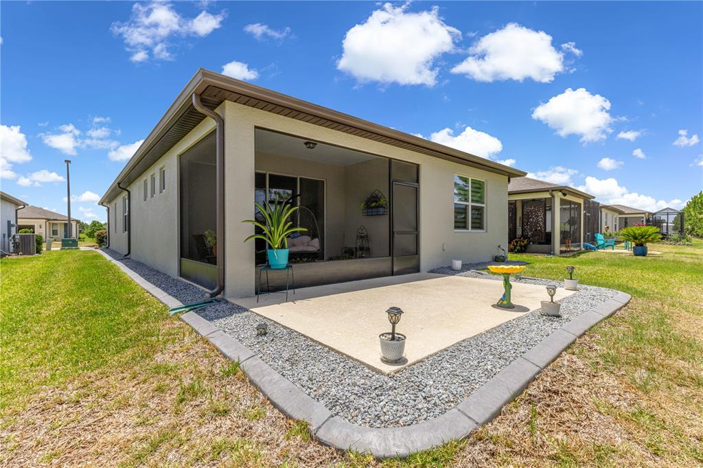 A tan house features a screened-in patio and a concrete slab with decorative landscaping stones — 5942 SW 93 CIRCLE, OCALA, FL