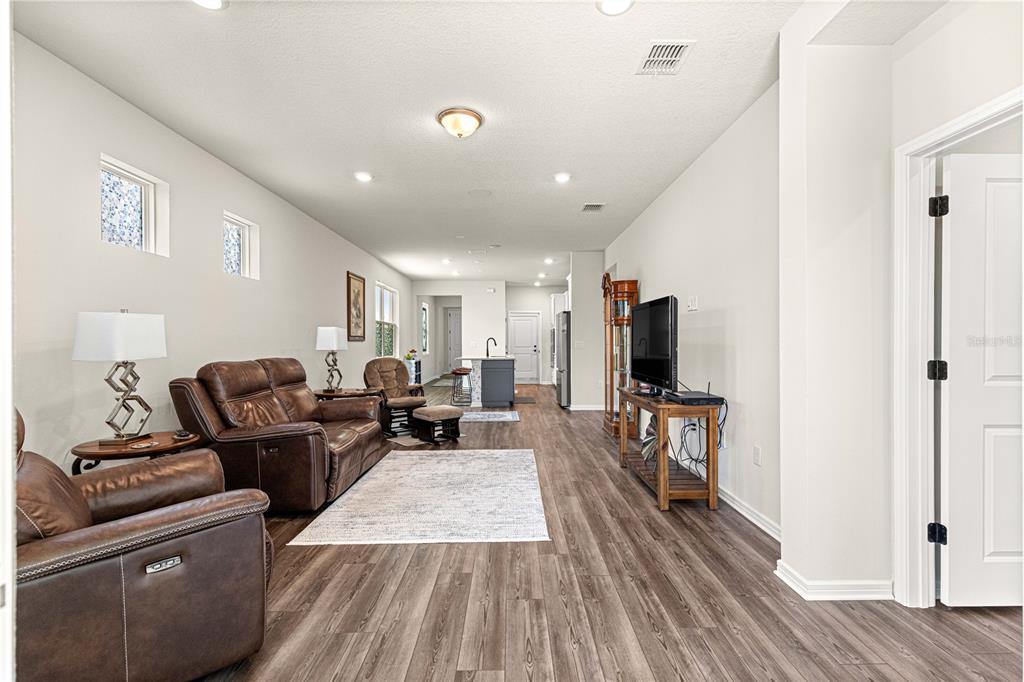 A living room with brown leather furniture, wood-look flooring, and an open kitchen beyond — 5942 SW 93 CIRCLE, OCALA, FL