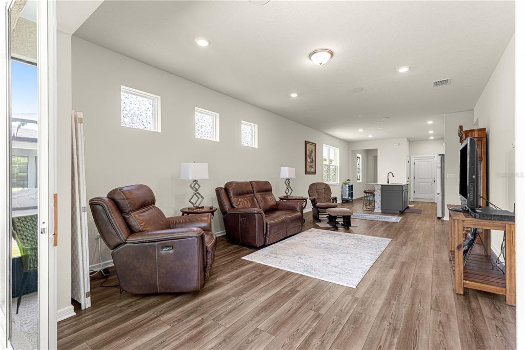 A living room with brown leather recliners, wood-look flooring, and an open kitchen in the background — 5942 SW 93 CIRCLE, OCALA, FL