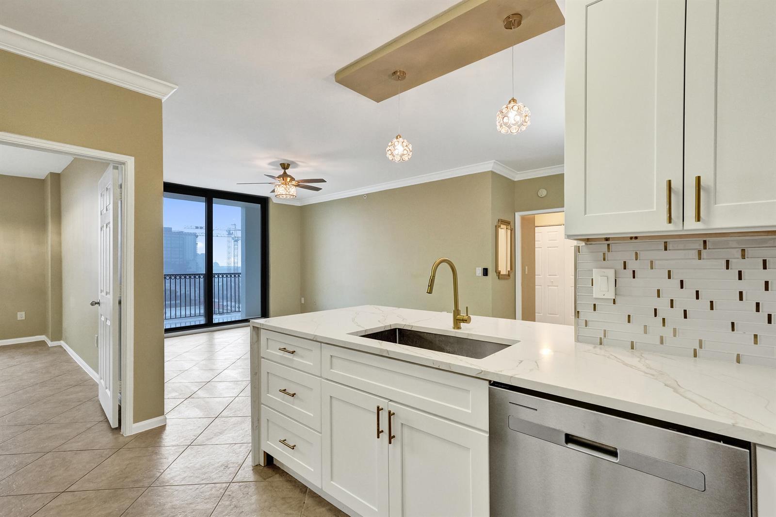 A kitchen island with a white countertop and gold faucet faces a living area — 651 Okeechobee Boulevard # 1010, West Palm Beach FL 33401, WEST PALM BEACH, FL