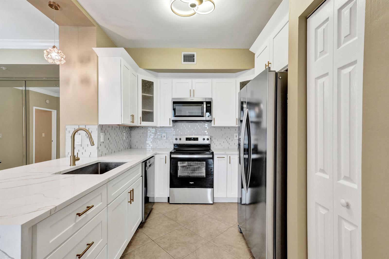 A kitchen features white cabinets, stainless steel appliances, a quartz countertop, and a tile backsplash — 651 Okeechobee Boulevard # 1010, West Palm Beach FL 33401, WEST PALM BEACH, FL