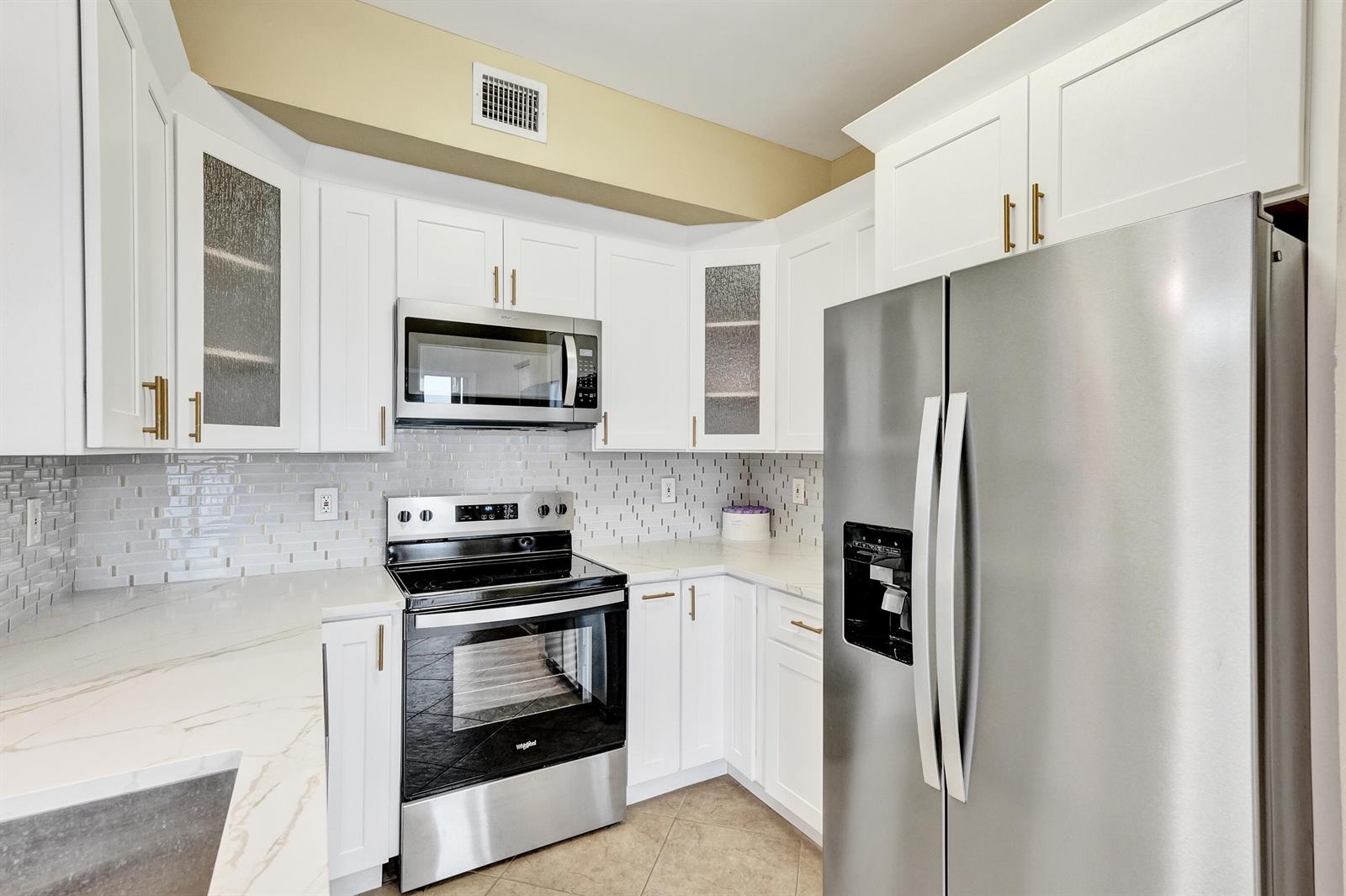 A kitchen features white cabinets, stainless steel appliances, a tiled backsplash, and light-colored countertops — 651 Okeechobee Boulevard # 1010, West Palm Beach FL 33401, WEST PALM BEACH, FL