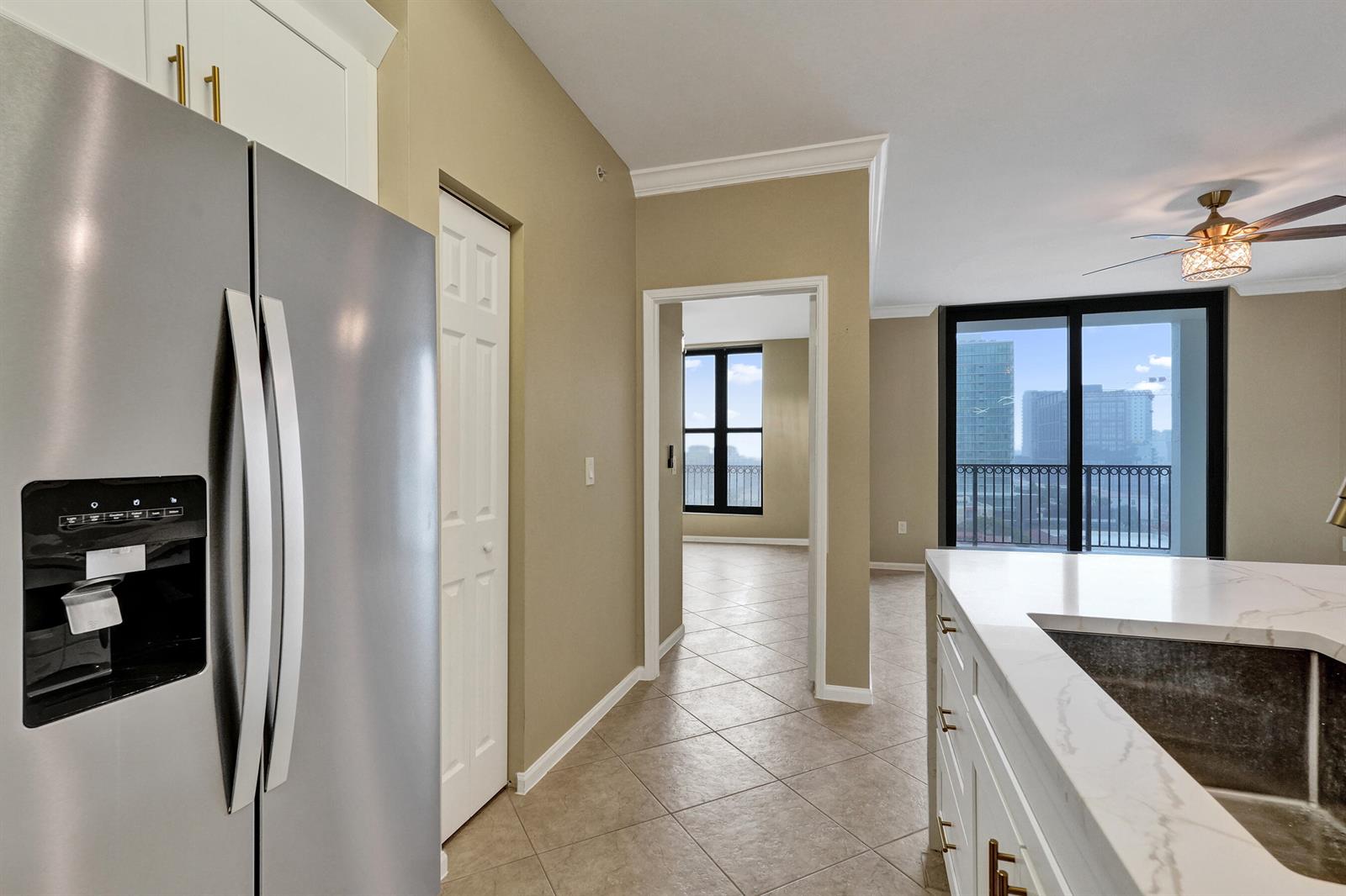 A kitchen with stainless steel appliances and white cabinets overlooks a living area with balcony — 651 Okeechobee Boulevard # 1010, West Palm Beach FL 33401, WEST PALM BEACH, FL