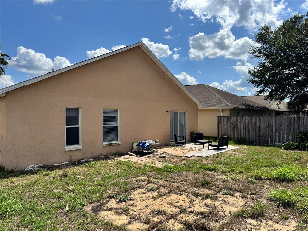 The rear exterior of a tan stucco house features two windows, a sliding glass door, and a patio — 260 PICCOLO WAY, DAVENPORT, FL