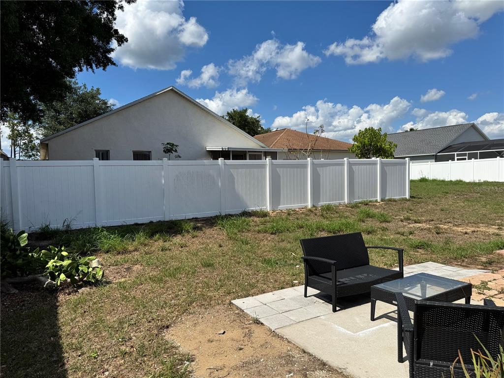 A backyard features a white vinyl privacy fence, a small concrete patio, and patio furniture — 260 PICCOLO WAY, DAVENPORT, FL
