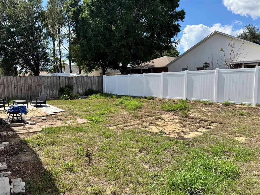 A backyard features a white vinyl fence, a wooden fence, and a small stone patio — 260 PICCOLO WAY, DAVENPORT, FL