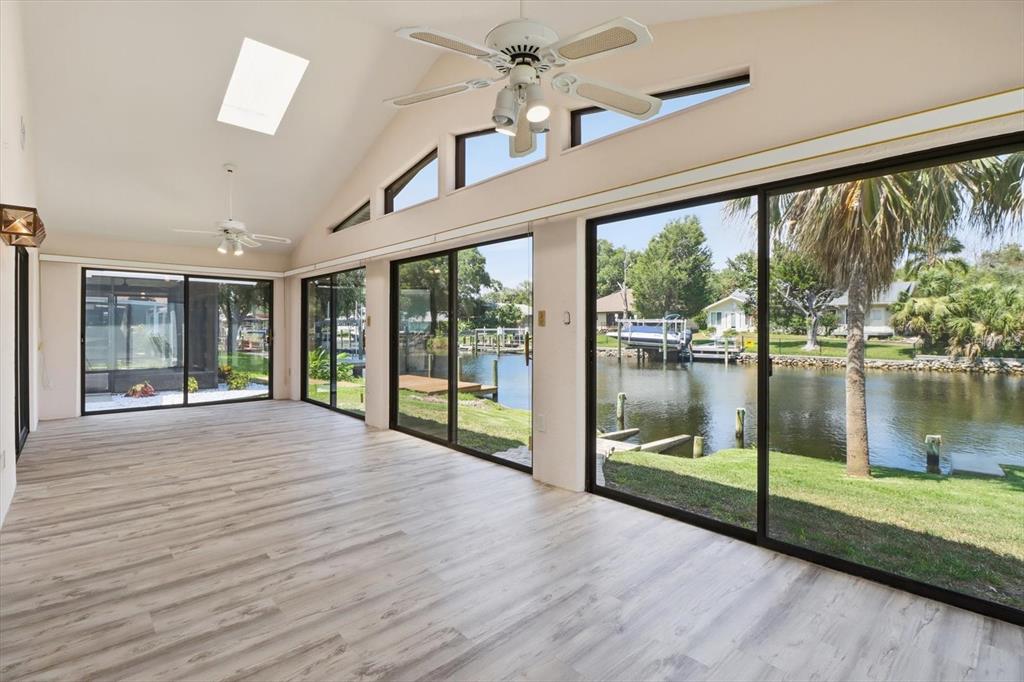 A sunroom with wood-look flooring, vaulted ceilings, and sliding glass doors overlooking a canal — 11621 W RIVERHAVEN DRIVE, HOMOSASSA, FL
