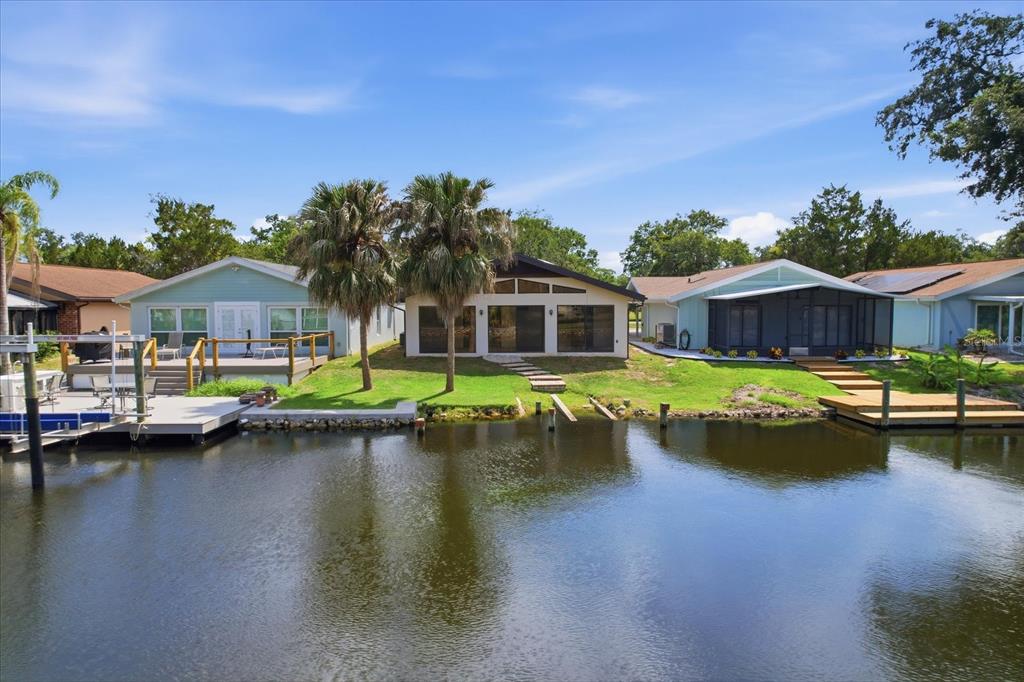 Three waterfront houses with docks and palm trees sit along a canal under a blue sky — 11621 W RIVERHAVEN DRIVE, HOMOSASSA, FL