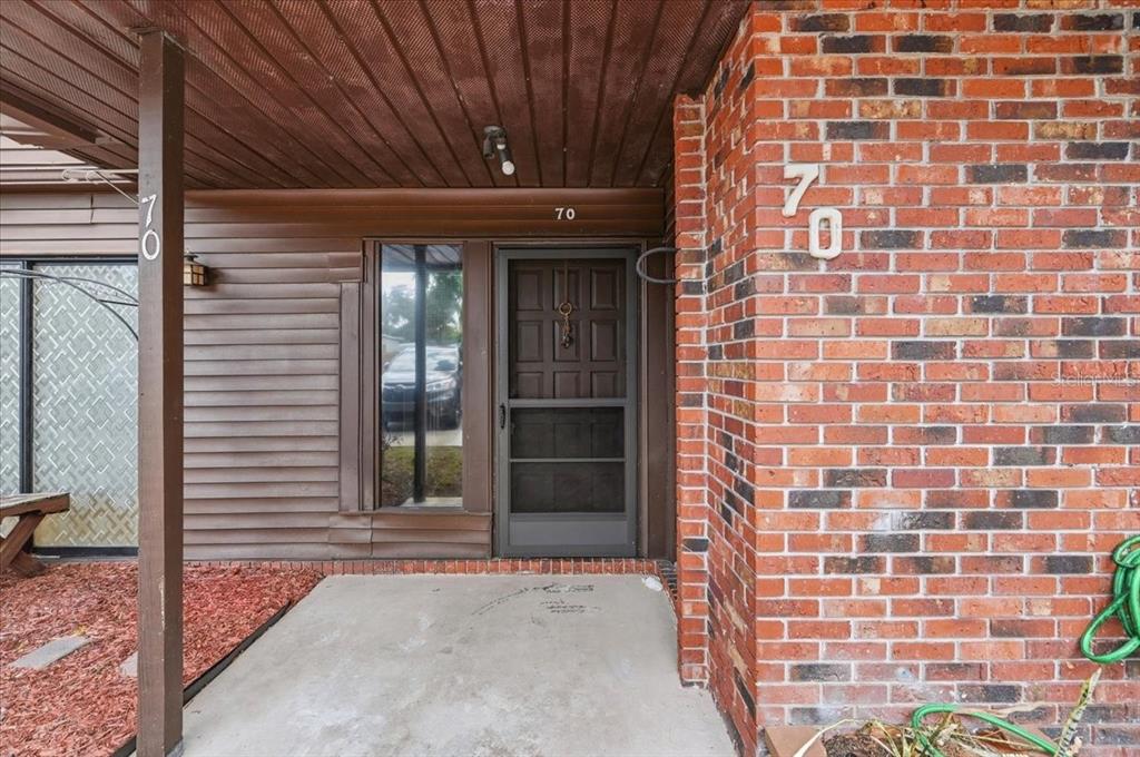 The exterior entrance features a brick wall, brown siding, a screen door, and a concrete porch — 1836 N CRYSTAL LAKE DRIVE UNIT 70, LAKELAND, FL