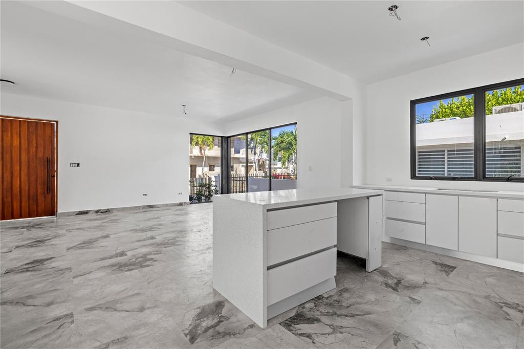 A modern kitchen and living area with white cabinets, a stone island, and marble flooring — 2058 CACIQUE, SAN JUAN, PR