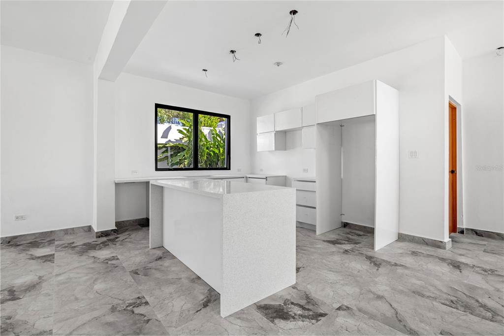 A modern kitchen features white cabinetry, a quartz island, and gray marble-patterned tile flooring — 2058 CACIQUE, SAN JUAN, PR