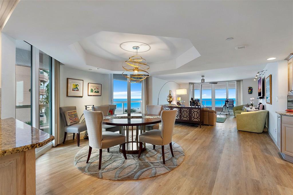 An open-concept dining and living area features light wood floors, a round table, and ocean views — 1310 GULF BOULEVARD UNIT 4-G, CLEARWATER, FL