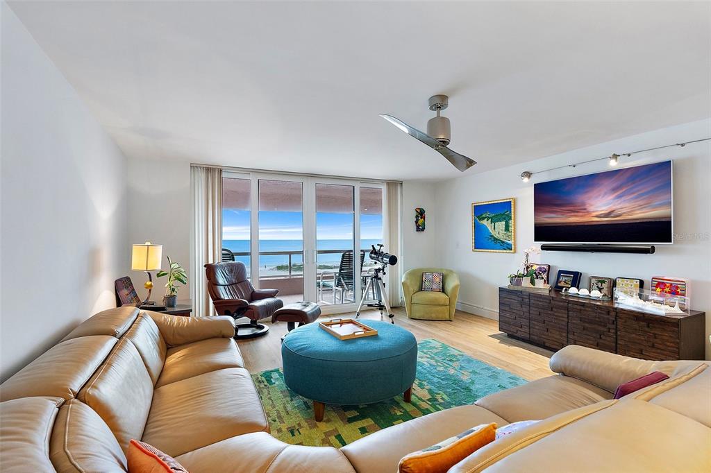 A living room features a leather sectional, a blue ottoman, and a balcony overlooking the ocean — 1310 GULF BOULEVARD UNIT 4-G, CLEARWATER, FL