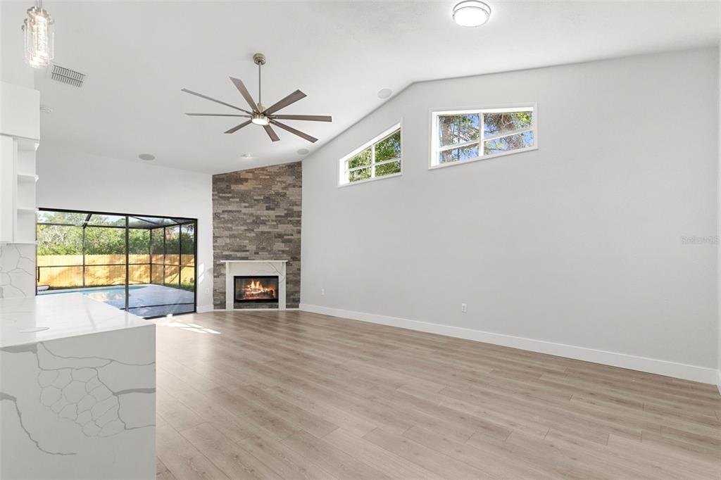 A living room features a stone fireplace, vaulted ceilings, light wood floors, and large windows — 11651 SUNSHINE POND ROAD, TAMPA, FL