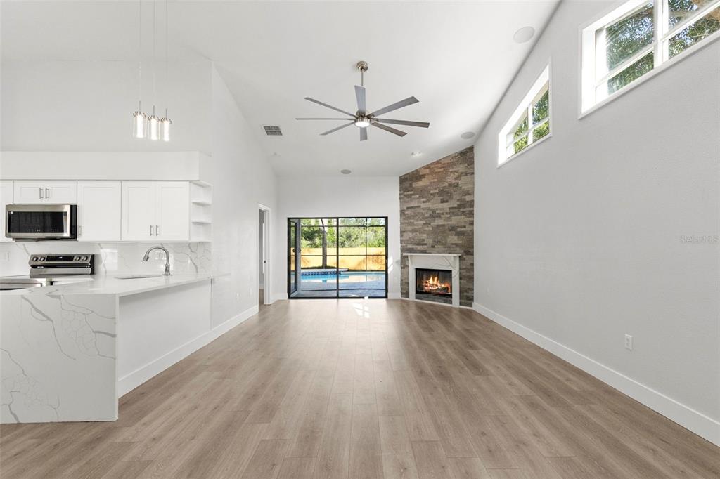 A modern open-concept living area features a stone fireplace, white kitchen cabinets, and pool views — 11651 SUNSHINE POND ROAD, TAMPA, FL