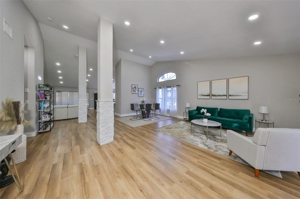 An open-concept living and dining area features light wood flooring, white columns, and vaulted ceilings — 9309 HAMPSHIRE PARK DRIVE, TAMPA, FL