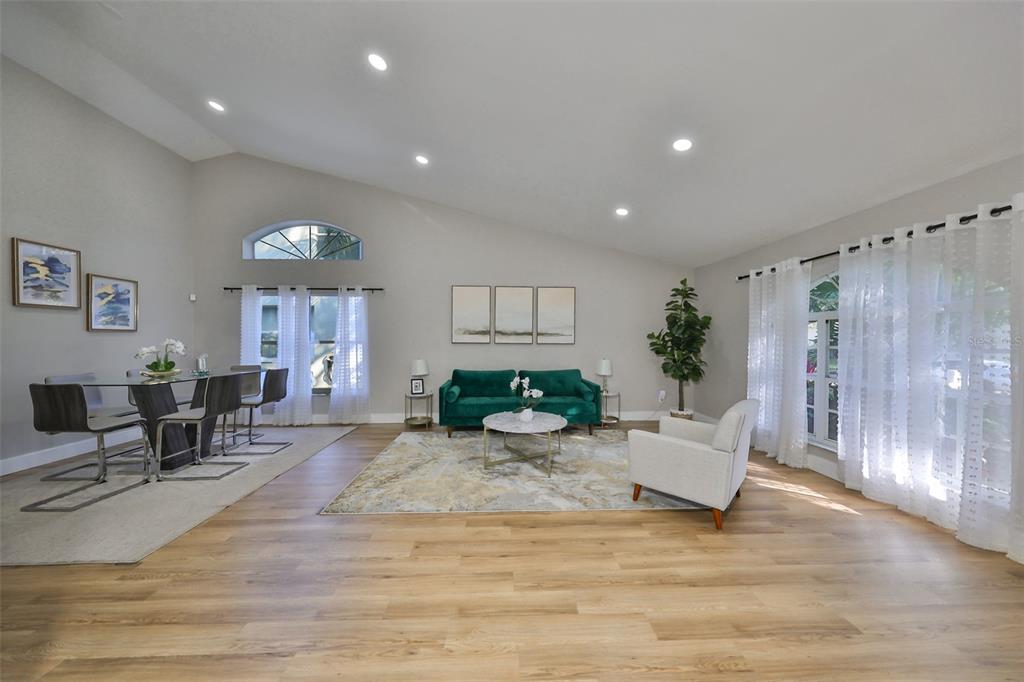 A spacious living and dining area with vaulted ceilings, light wood flooring, and large windows — 9309 HAMPSHIRE PARK DRIVE, TAMPA, FL