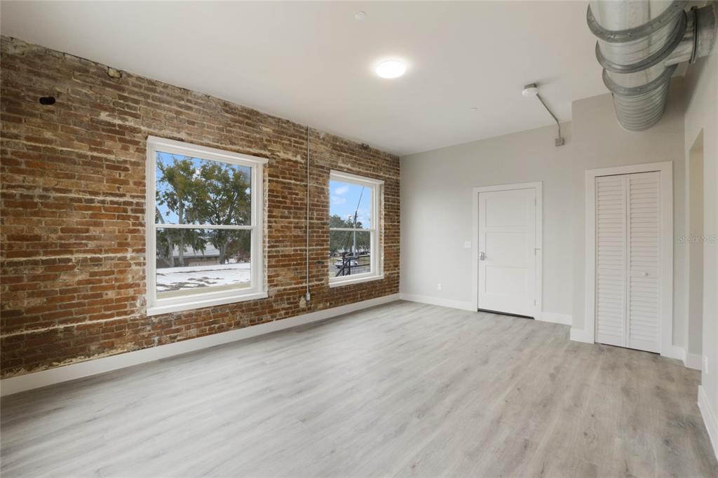 An empty room features exposed brick walls, light wood-look flooring, and an exposed ceiling duct — 792 W MONTROSE STREET UNIT 205, CLERMONT, FL